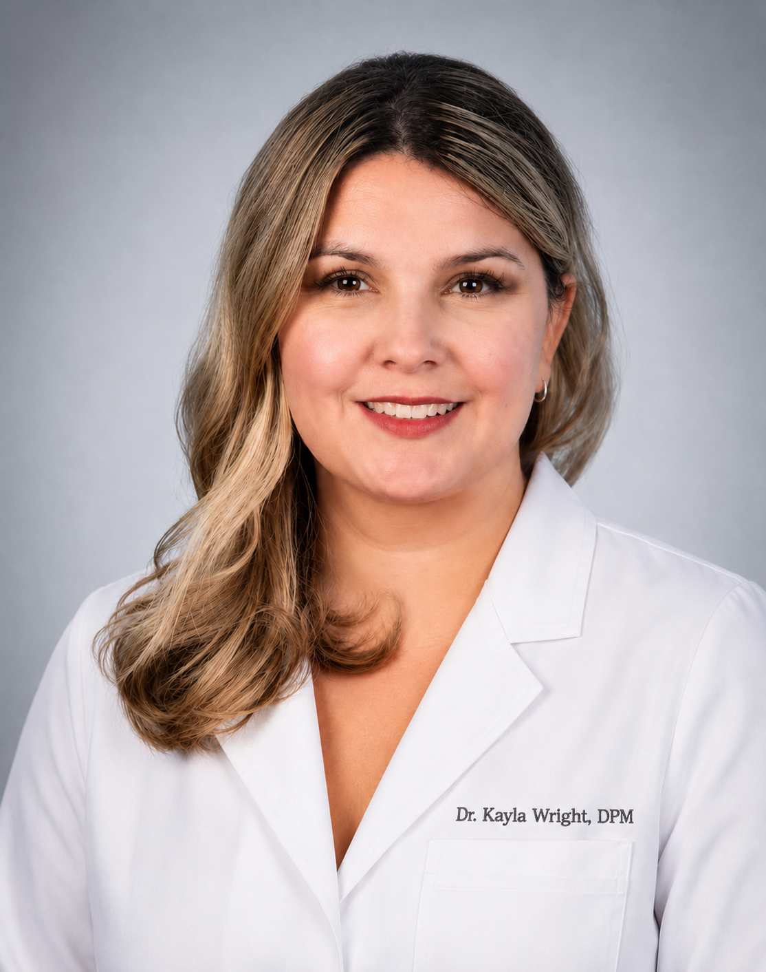 Portrait of Dr. Kayla Wright, DPM, Foot & Ankle Surgeon, standing in a white coat embroidered with her name.