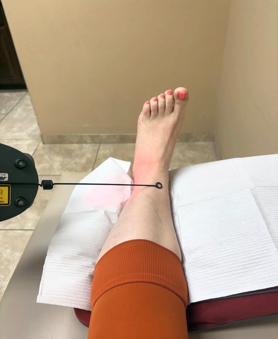 A patient's foot and ankle resting on an exam table while an MLS® Laser Therapy handpiece is positioned above the ankle during an in-office treatment session.